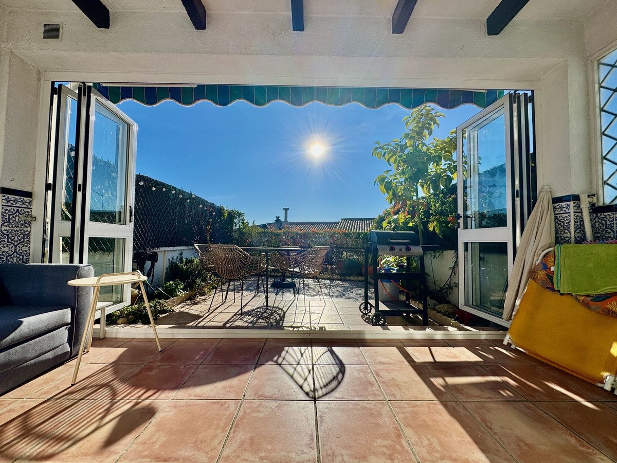 Sunny terrace with outdoor seating, grill, and bi-fold doors opening to a bright blue sky and greenery.