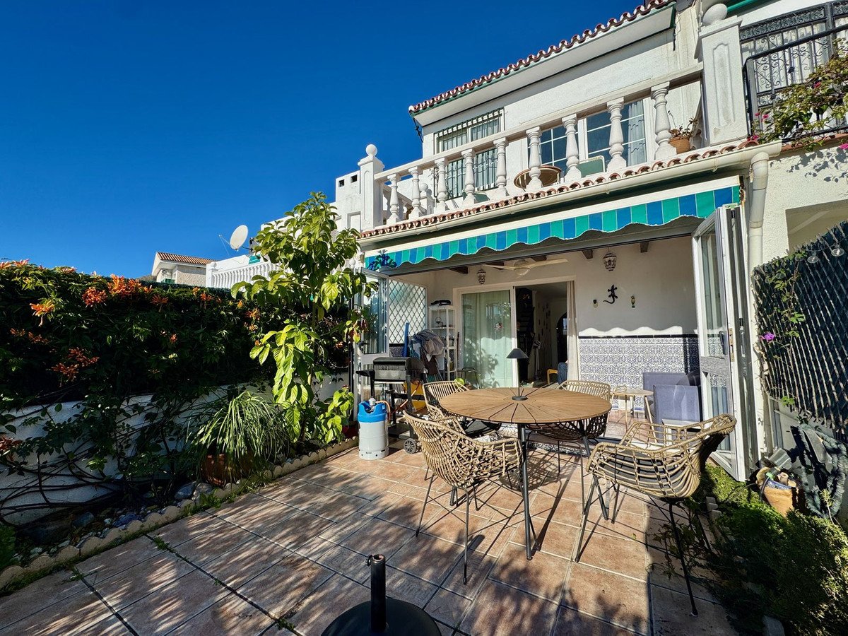 Terrace with outdoor dining set, barbecue, and lush greenery under a bright blue sky.