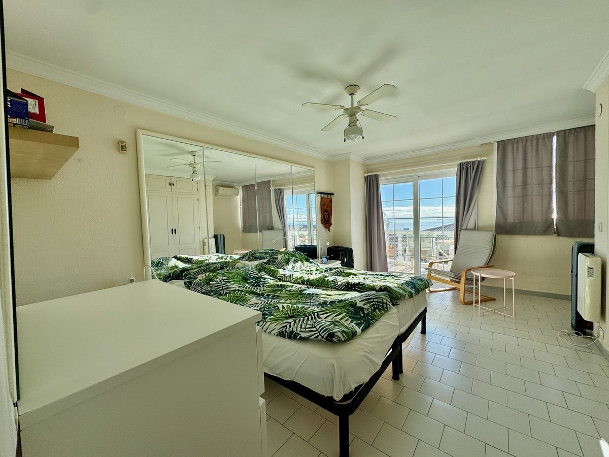 Bedroom with a large bed, mirrored wardrobe, ceiling fan, and sliding doors leading to a balcony with a sea view.
