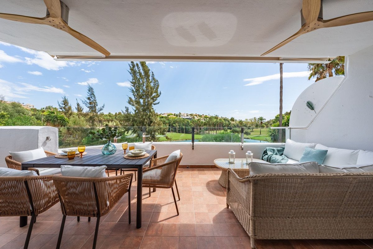 Spacious terrace with dining and lounge areas overlooking a lush golf course on a sunny day.