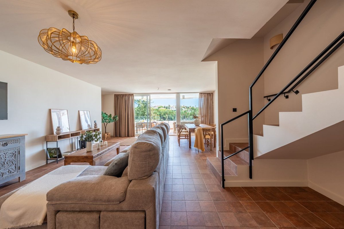 A spacious living and dining area with a large sofa, dining table, and sliding glass doors opening to an outdoor view.