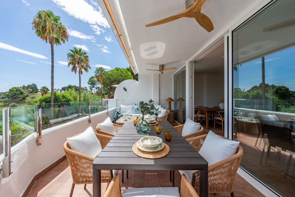A spacious terrace with a dining table and chairs overlooking palm trees and a golf course.