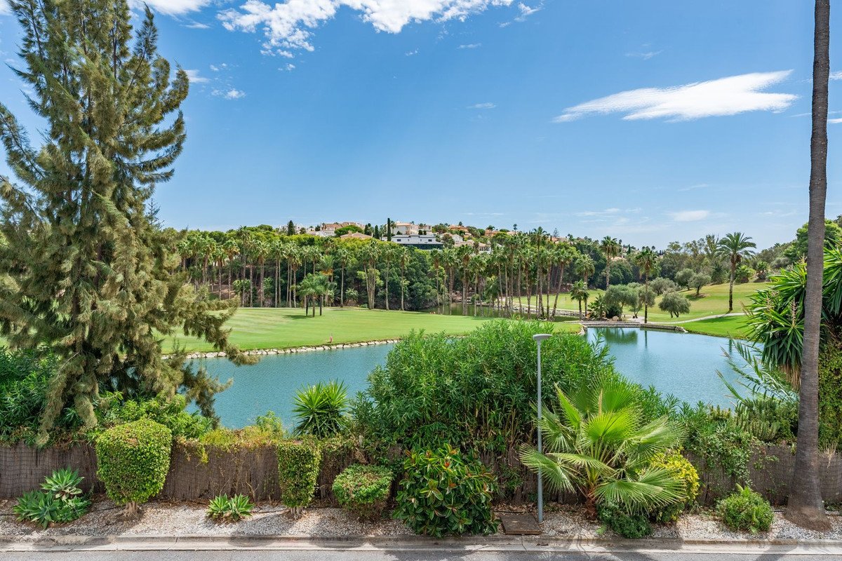 View from a terrace overlooking a serene lake on a lush golf course with palm trees and villas in the background.