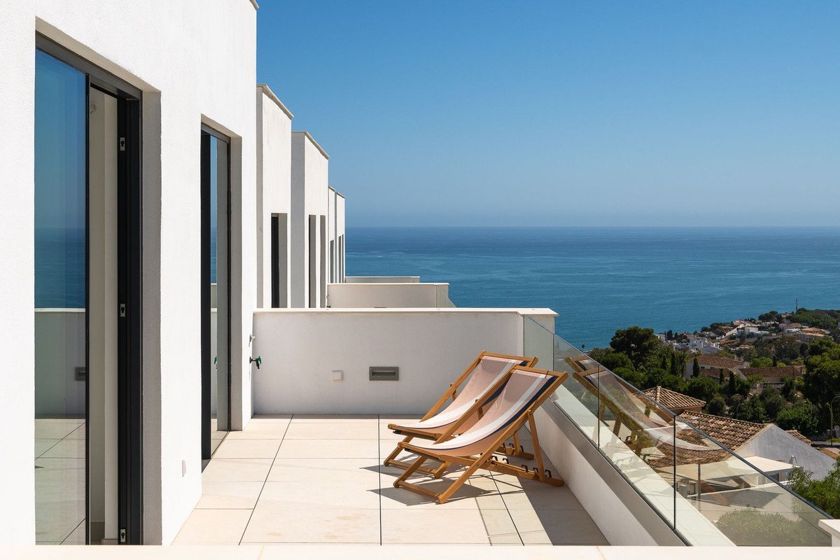 Modern terrace with lounge chairs and stunning sea view overlooking a town.