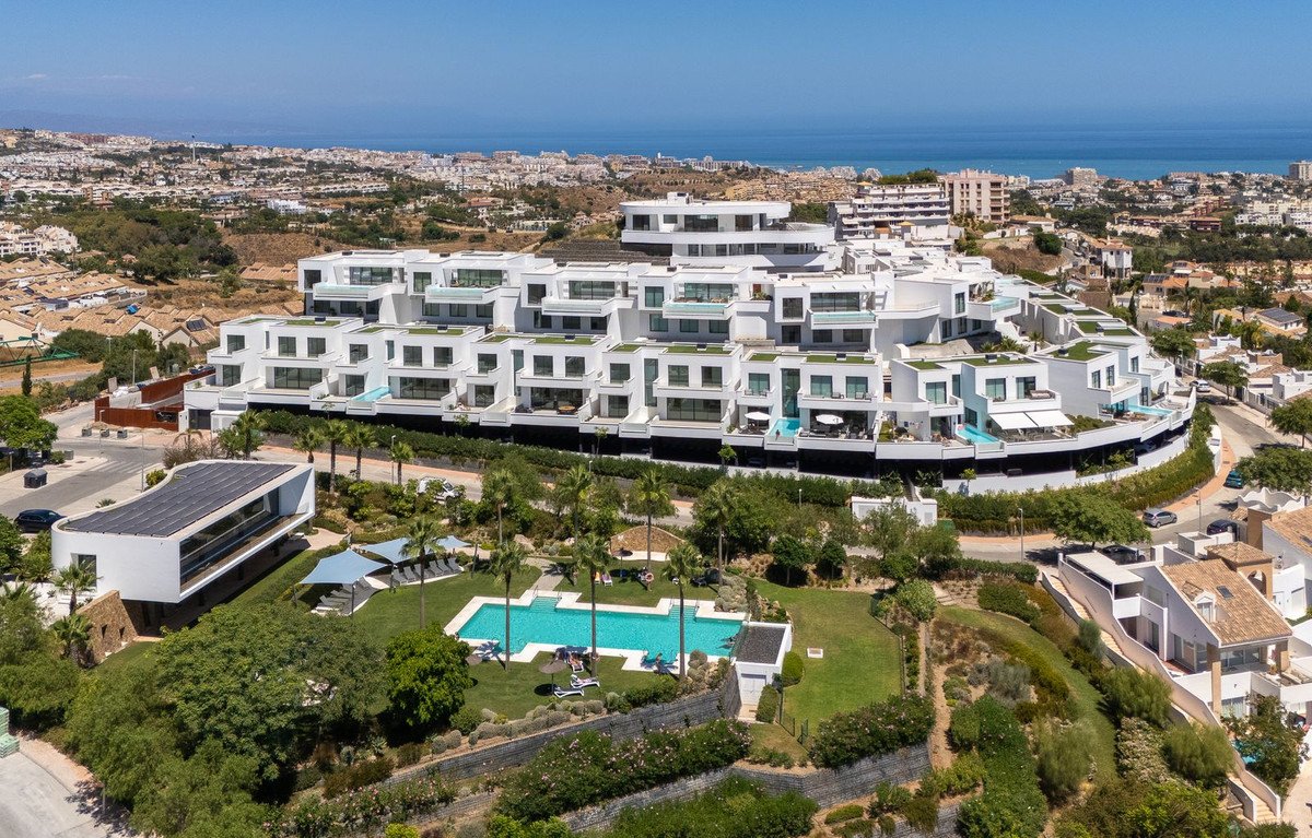 Modern white apartment complex with balconies, pools, and sea views in a sunny landscape.