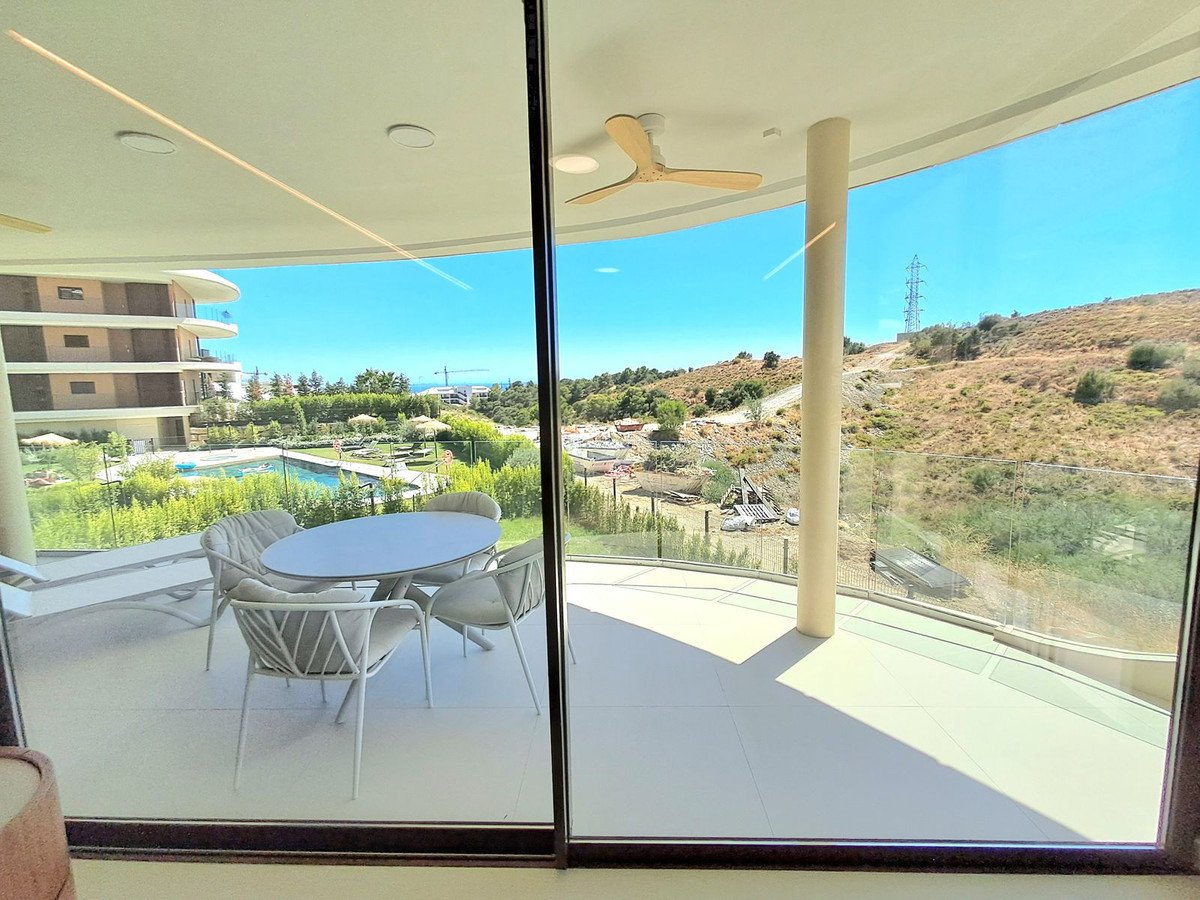 Modern balcony with outdoor dining set overlooking a swimming pool and distant hillside landscape under a clear blue sky.