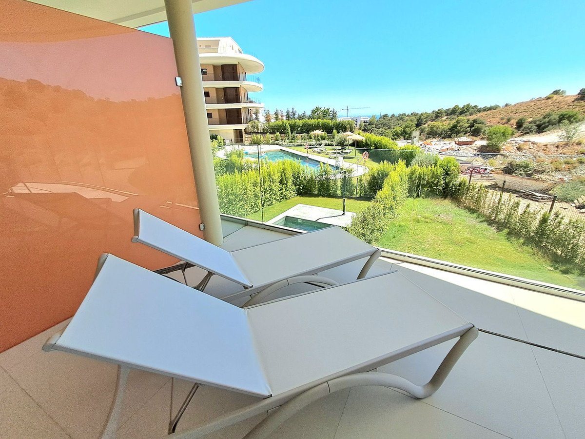 Two white lounge chairs on a balcony overlooking a swimming pool and landscaped garden on a sunny day.