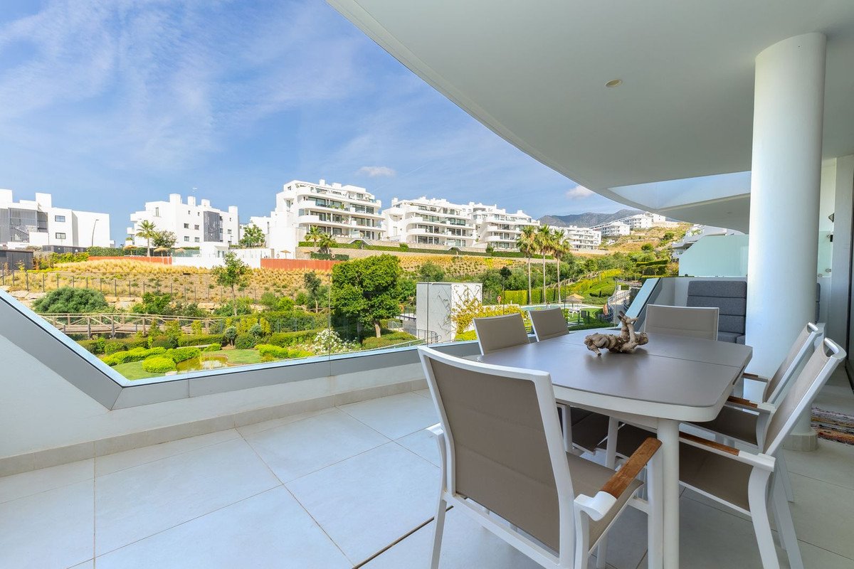 Terrace with dining table and chairs, overlooking lush gardens and modern apartment buildings.