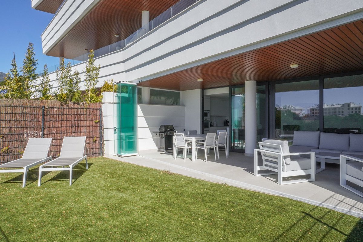 Modern terrace with outdoor dining set, grill, lounge chairs, and lawn, overlooking a building.