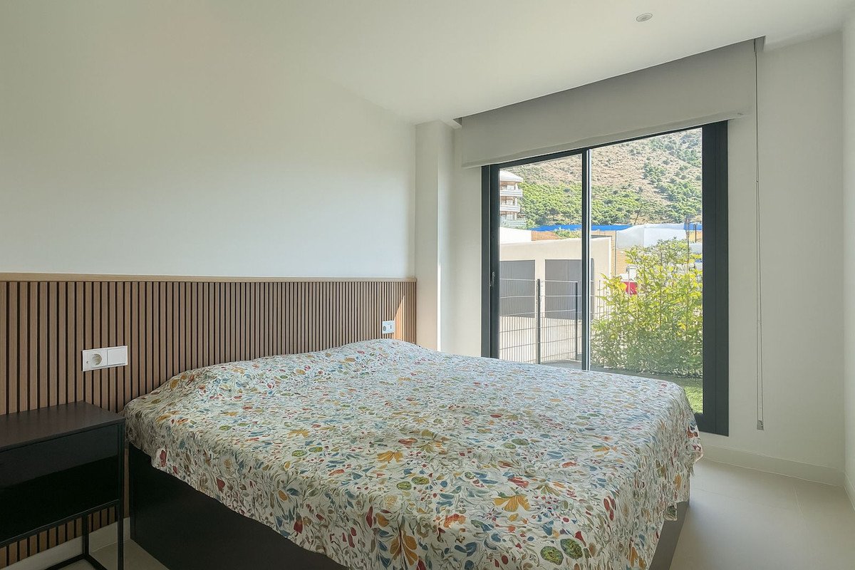 Bedroom with a large bed and floral duvet, featuring a floor-to-ceiling window with mountain views and natural light.