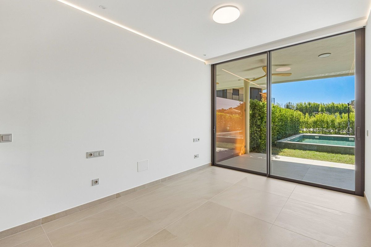 Modern room with large sliding glass doors revealing a view of a private swimming pool and lush green garden under a bright blue sky.