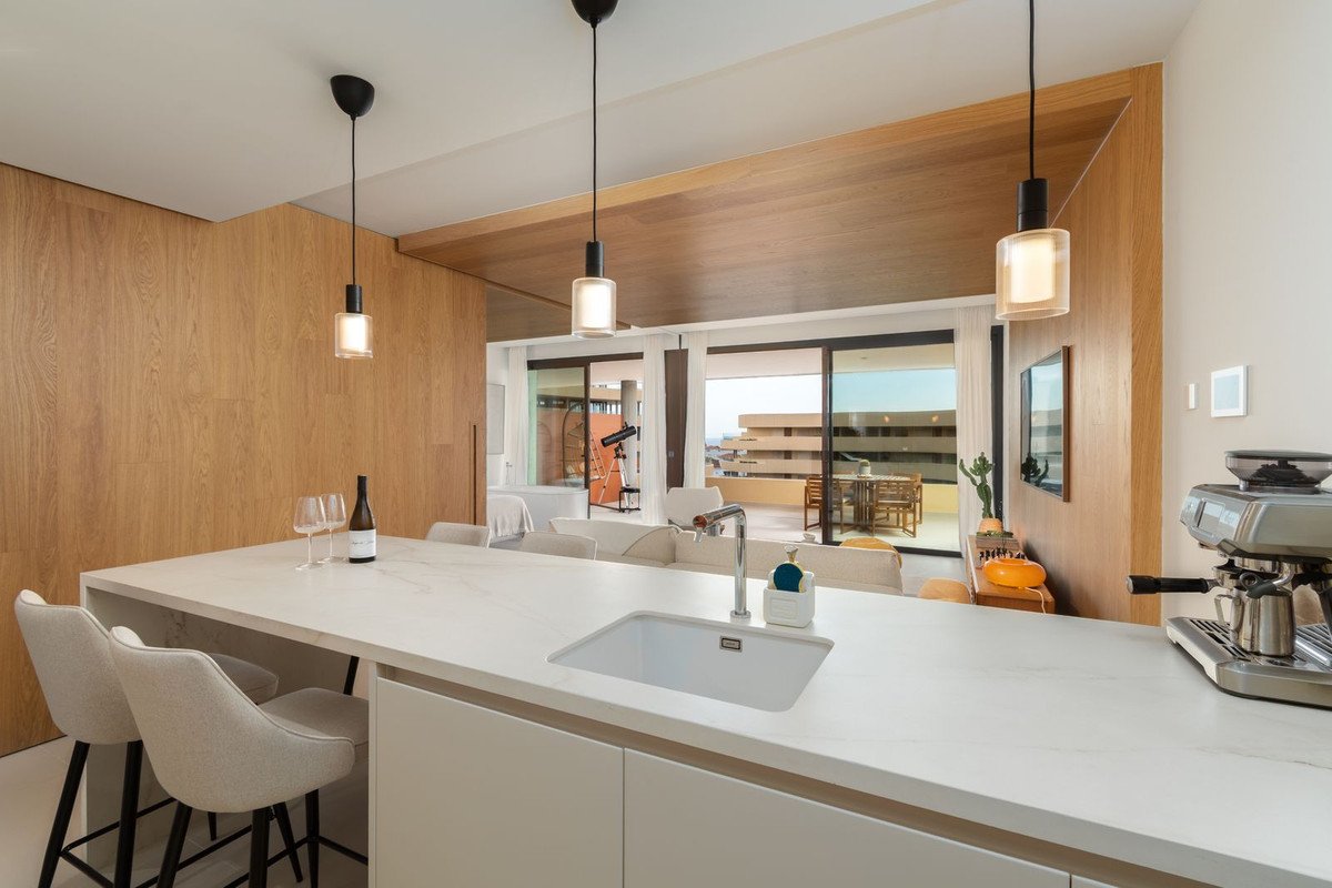 Modern kitchen with island, bar stools, and a view of a balcony with outdoor seating and city skyline.