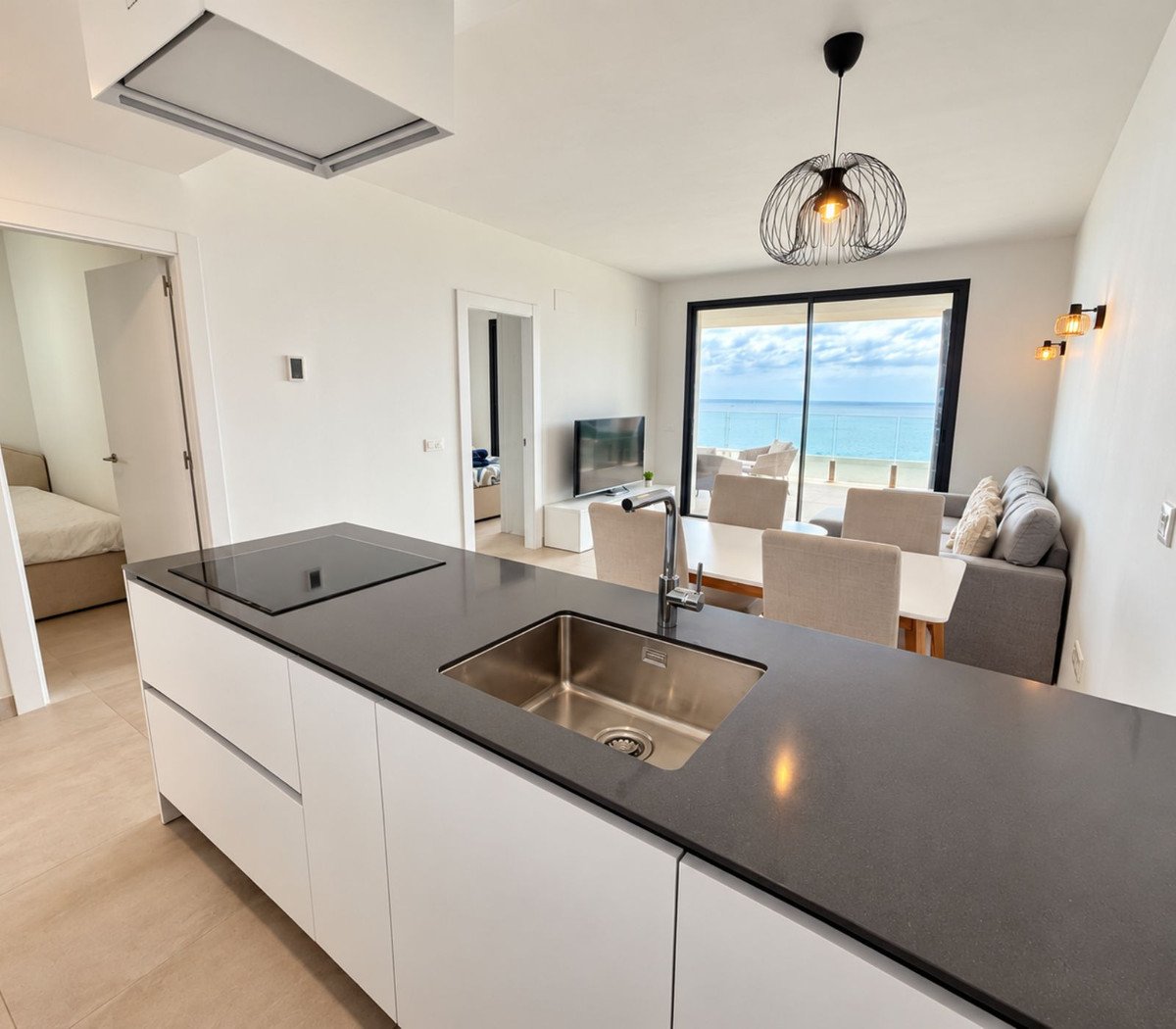 Modern kitchen island with sink, dining area, sofa, and a beautiful sea view through large windows.