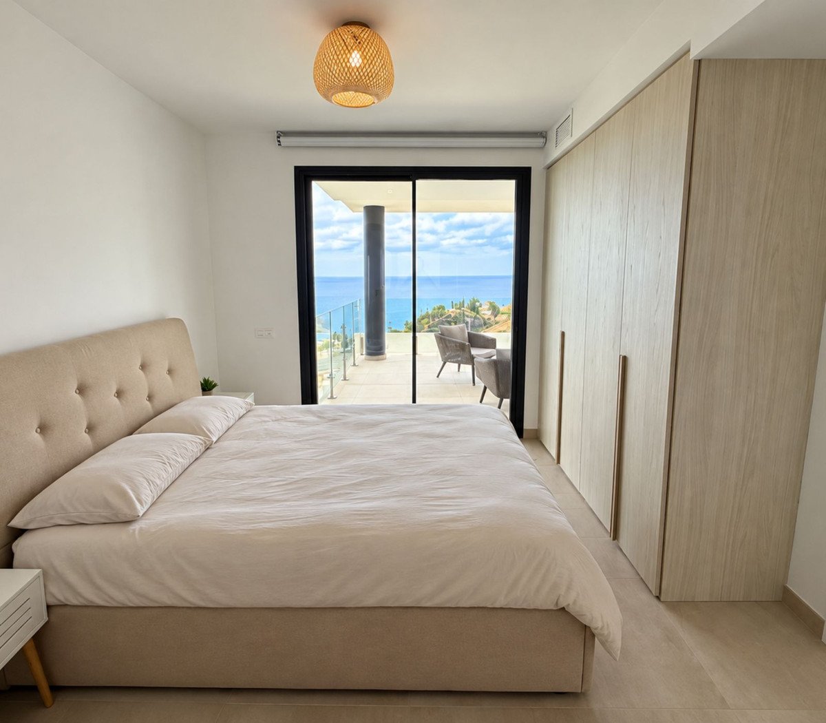 Bedroom with a large bed, a wardrobe, and a sliding glass door leading to a balcony with a sea view.