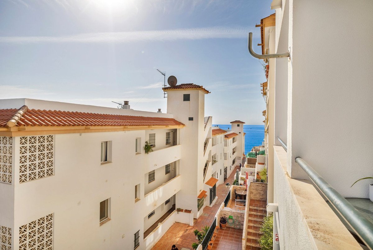 White buildings with orange tile roofs leading to a bright blue sea on a sunny day.