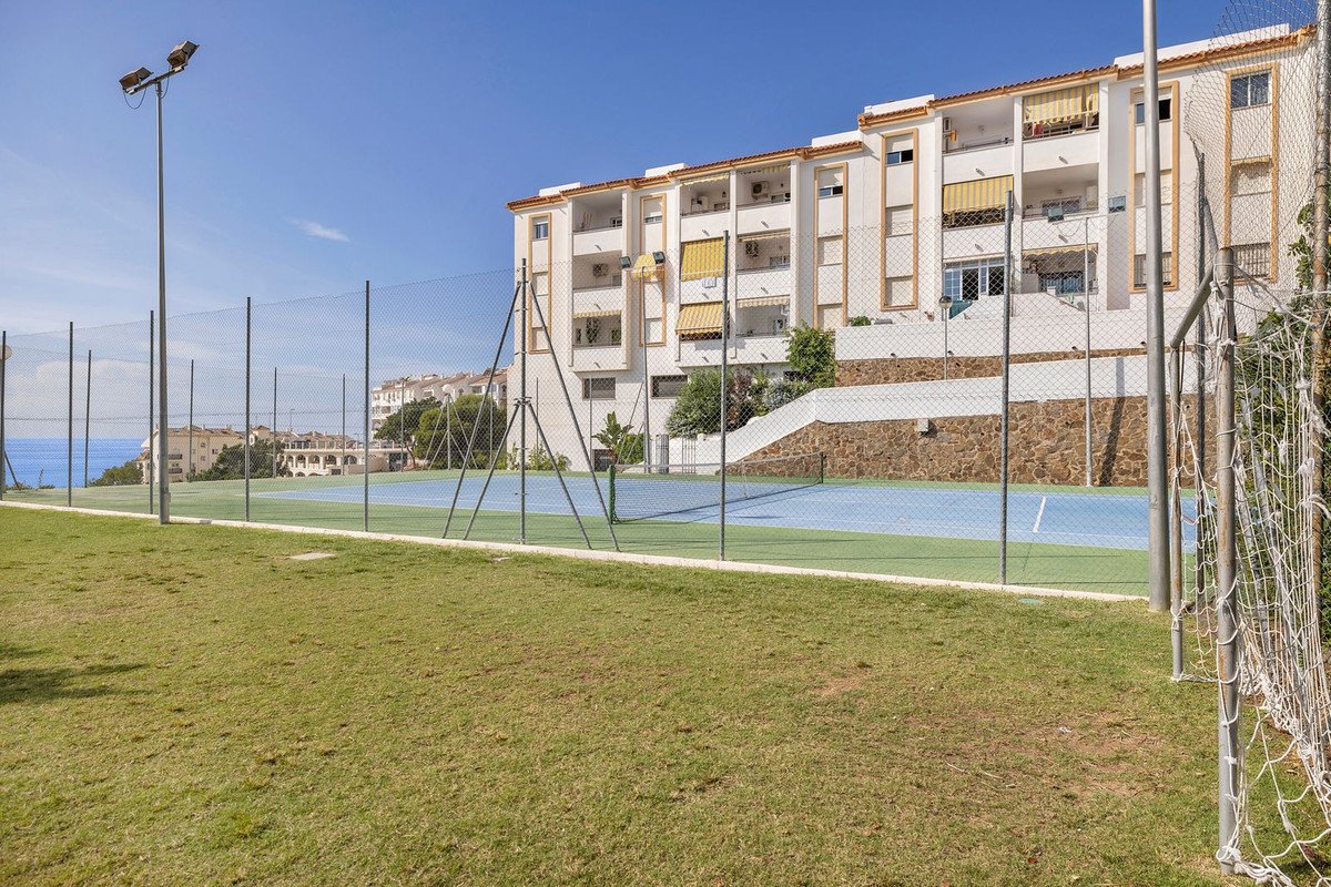 Tennis court with a sea view and apartments in the background on a sunny day.