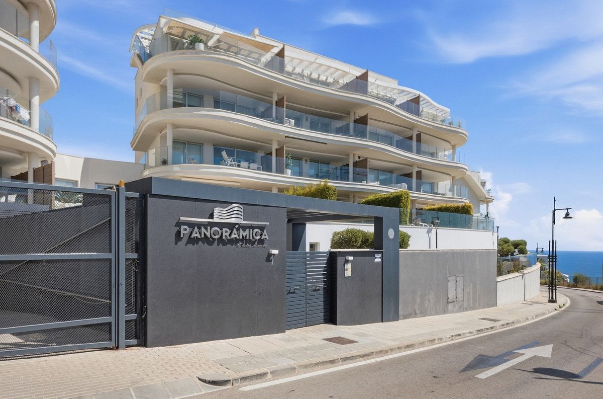 Exterior of a modern apartment building with curved balconies and sea views. Entrance gate with "Panorámica" signage.