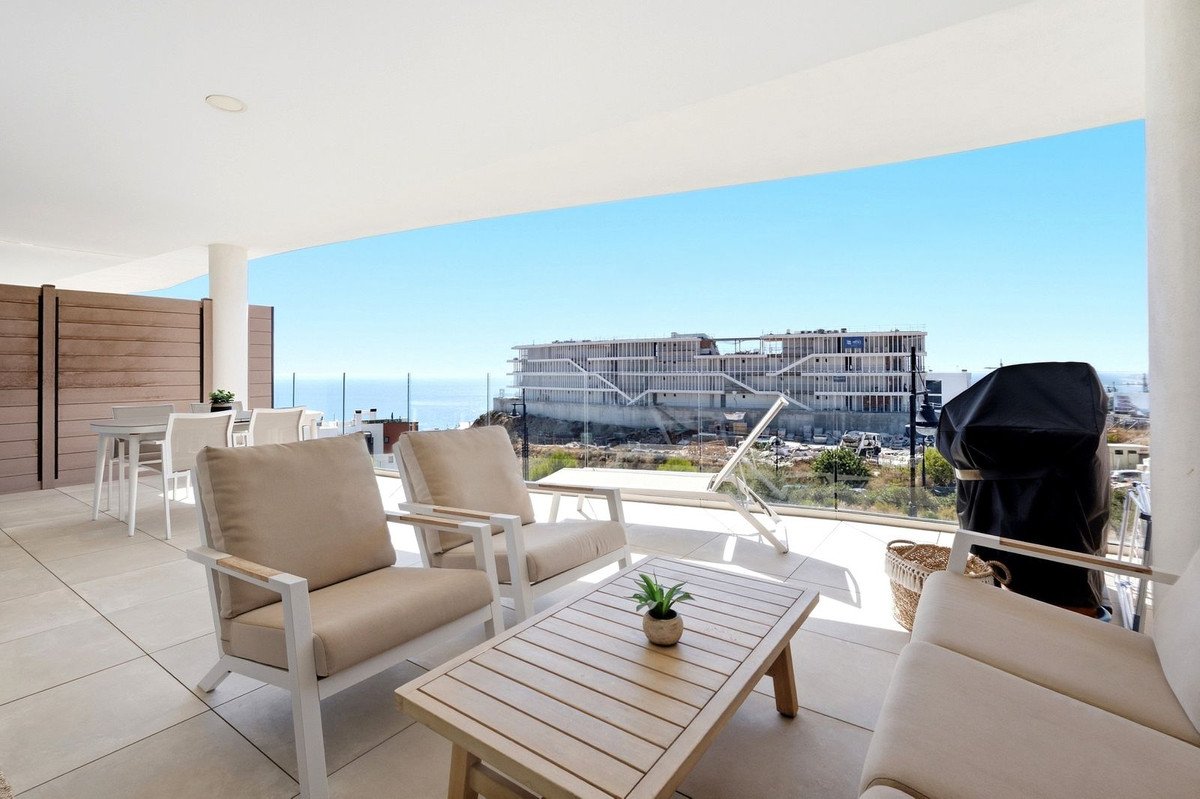 Spacious patio with outdoor furniture, grill, and a stunning view of the ocean and a building under construction.