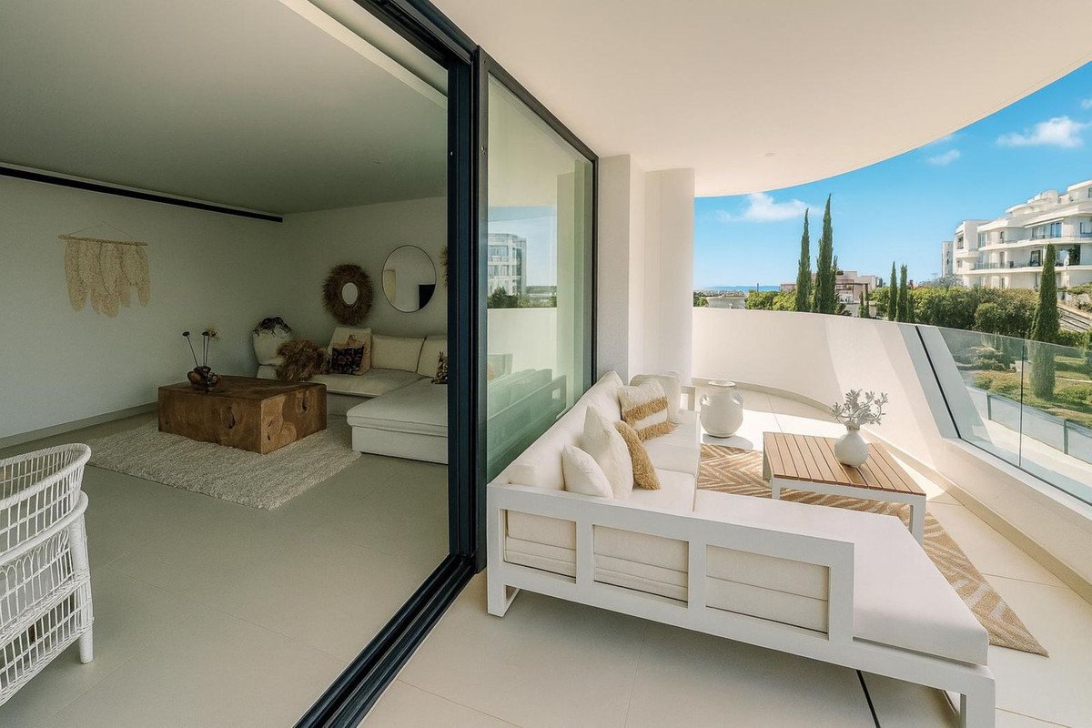 Modern living room with sofa and large sliding glass doors opening to a balcony with comfortable seating and scenic views.