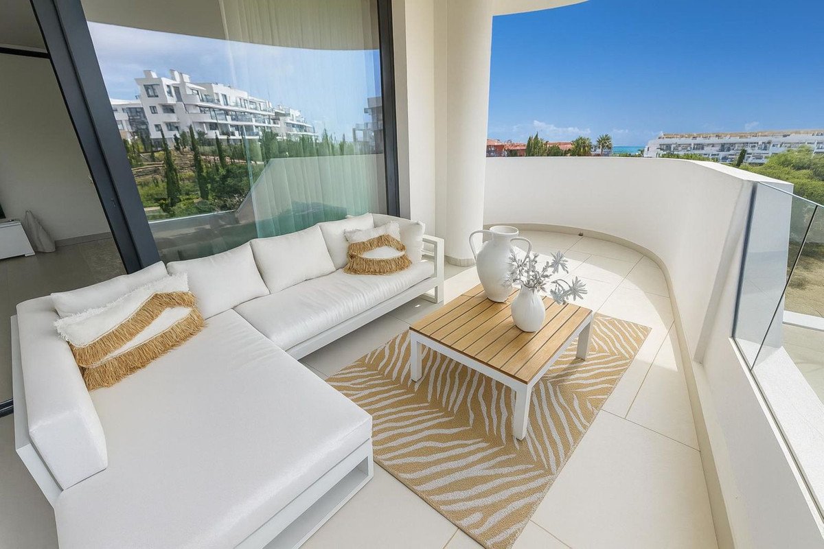 Modern balcony with white sectional sofa, coffee table, and sea view.