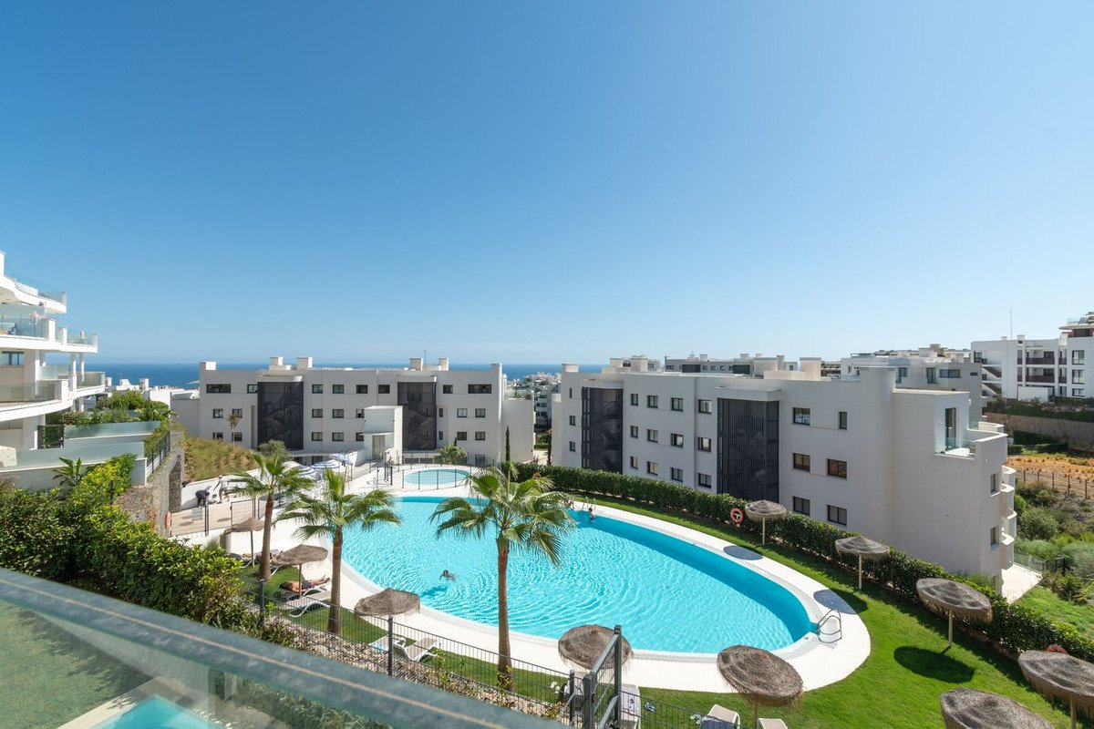 Resort complex with a large swimming pool, palm trees, and sea view under a clear blue sky.