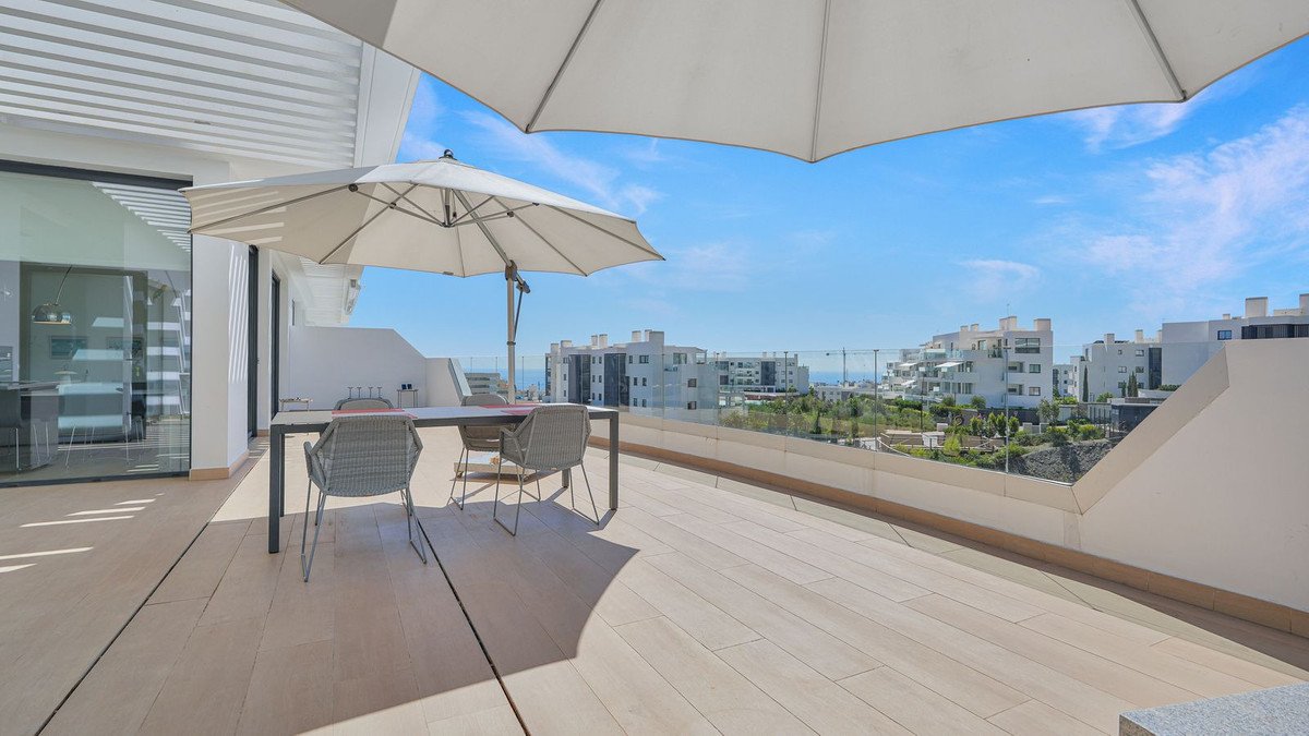 Spacious terrace with dining set and umbrellas, offering panoramic sea and apartment views under a clear blue sky.