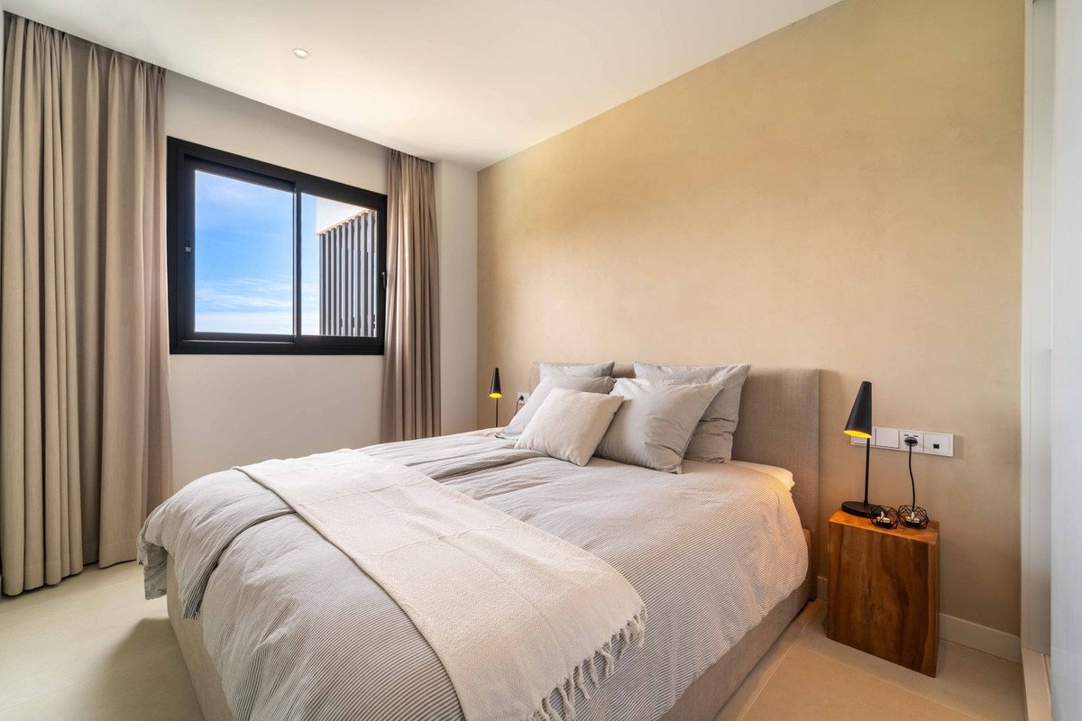 Modern bedroom with a large bed, neutral colors, and a window offering a sea view.