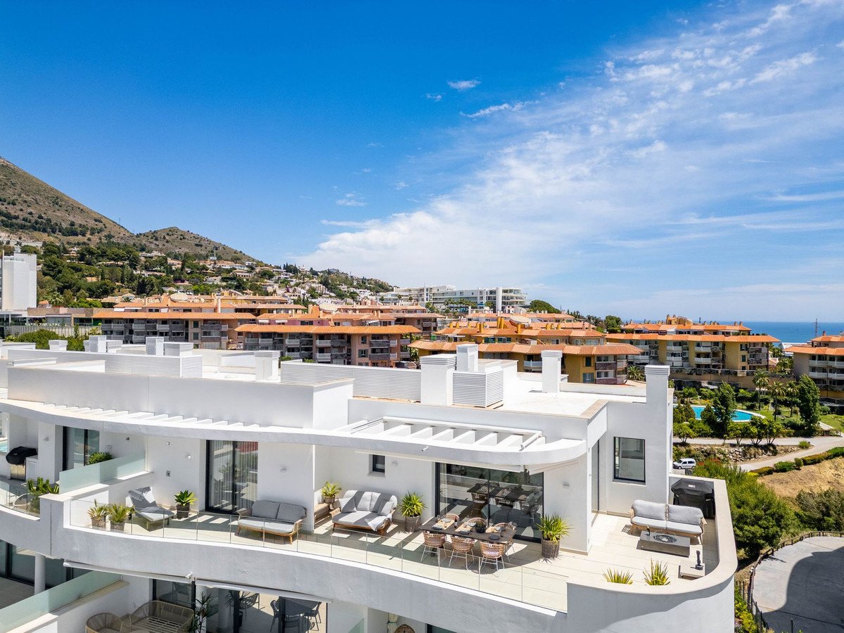 Modern apartment terrace with seating areas and outdoor dining overlooking the sea and mountains.