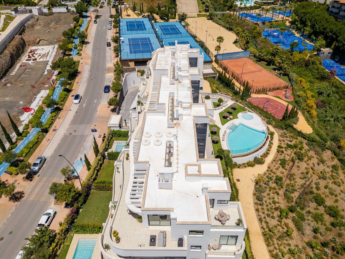 Aerial view of a modern building with a pool and tennis courts nearby, showcasing outdoor amenities and architecture.