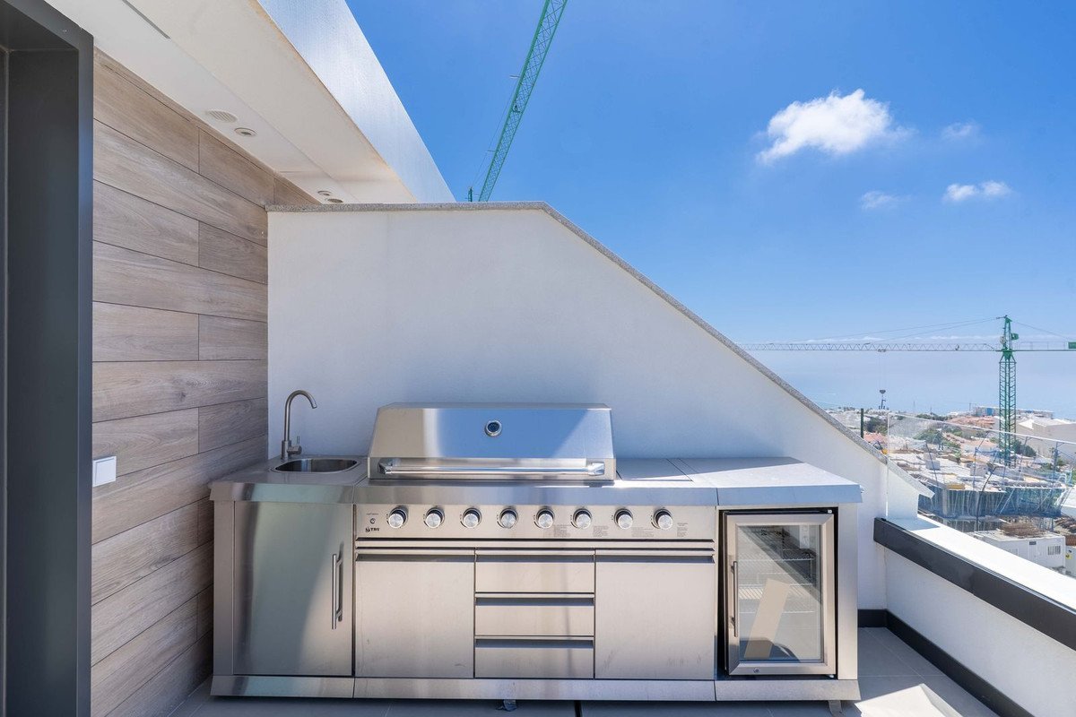 Rooftop outdoor kitchen with stainless steel grill, sink, and city view