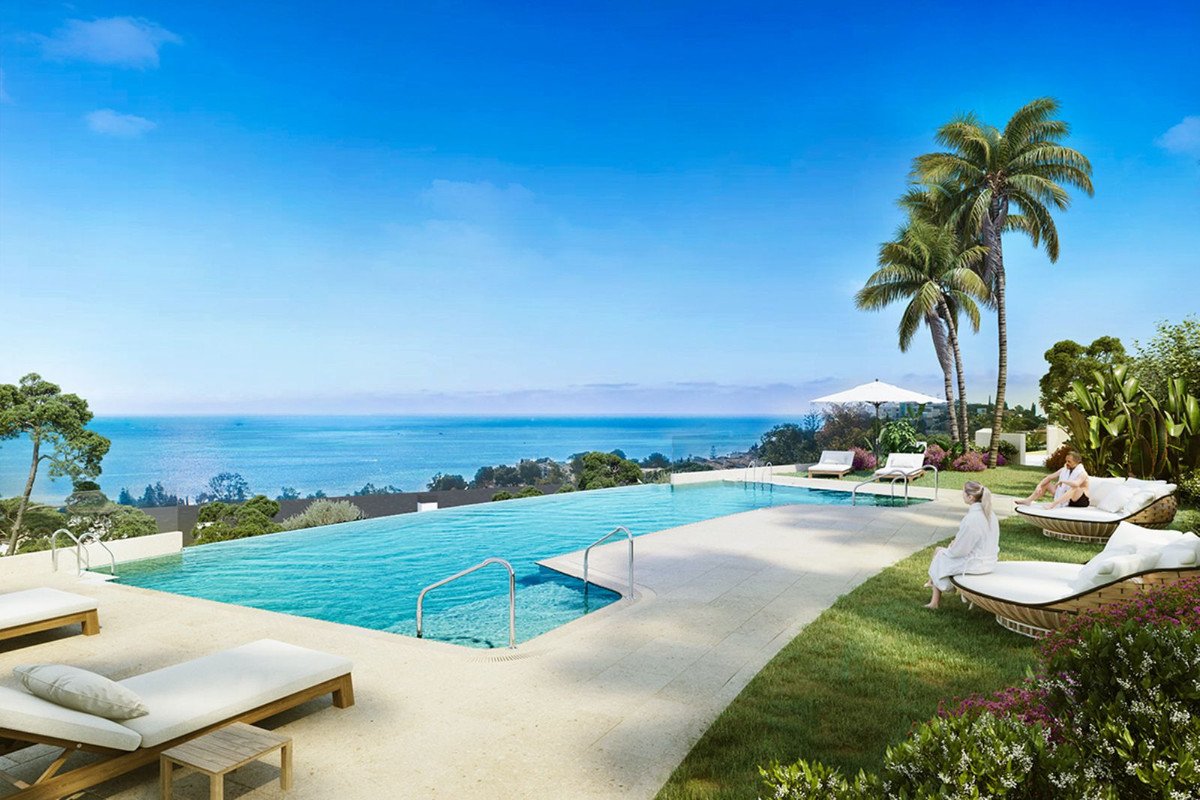 Infinity swimming pool with lounge chairs and lush greenery, overlooking a stunning sea view and coastline.