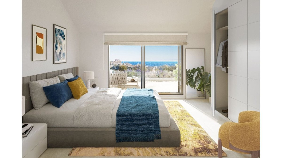 Modern bedroom with a large window offering stunning sea views and access to a private balcony with outdoor seating.