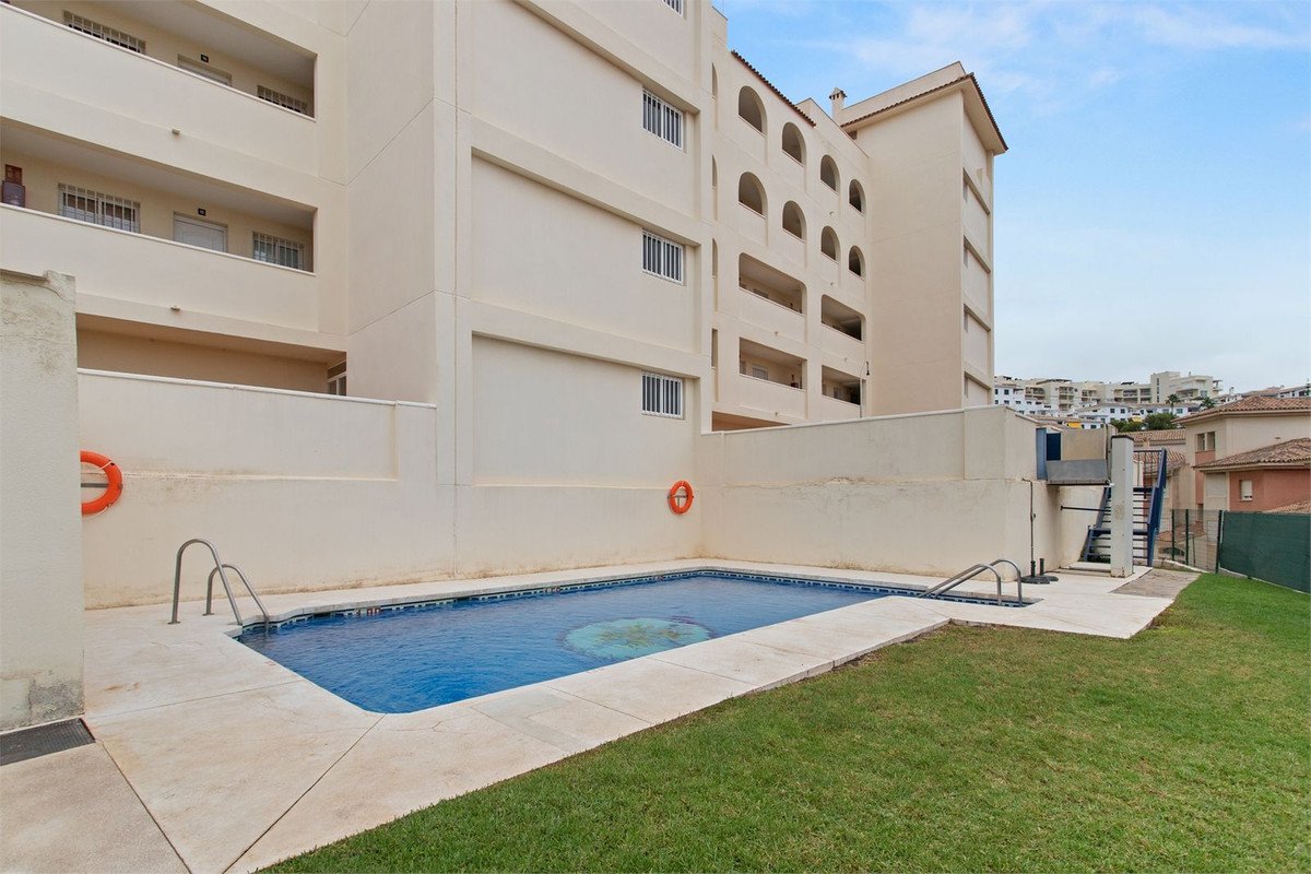 Communal swimming pool with surrounding lawn and apartment building in the background. Features rescue rings.