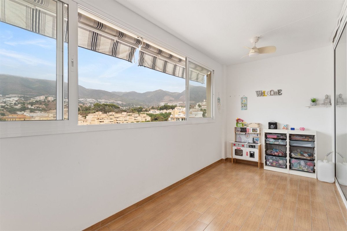 A room with a large window showing a view of mountains and a town, featuring children's toys and storage units.