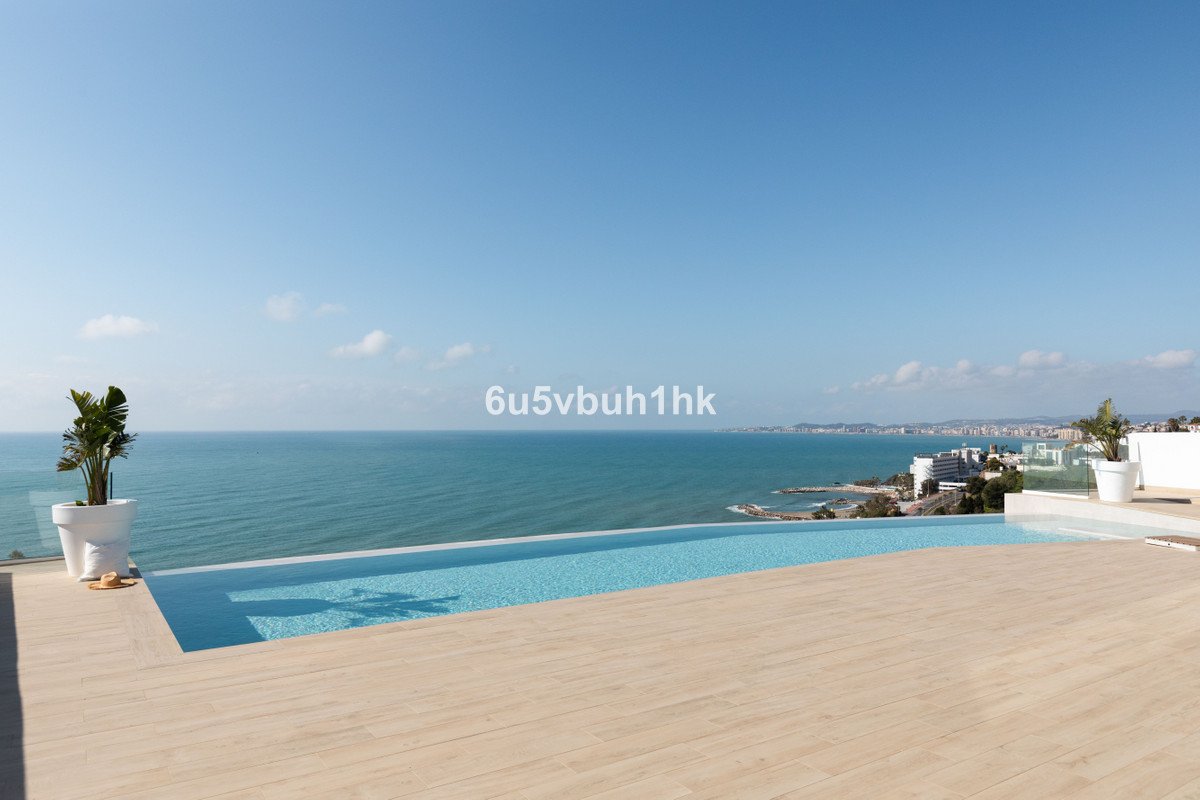A modern infinity pool on a wooden deck overlooking the ocean with a distant coastal town visible.