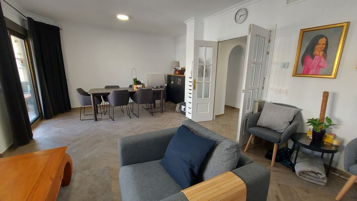 A modern living and dining room with grey furniture, a large window with black curtains, and a painting on the wall.