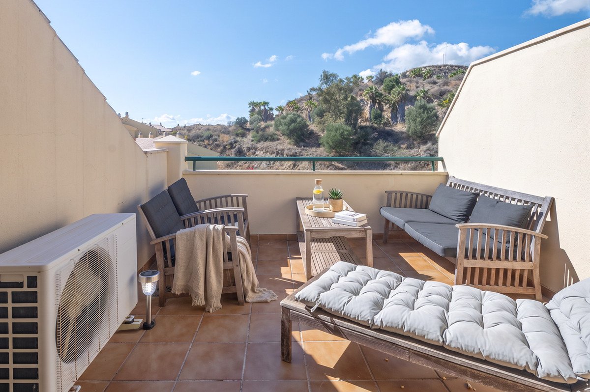 Sunny rooftop terrace with seating, cushions, and scenic hillside views
