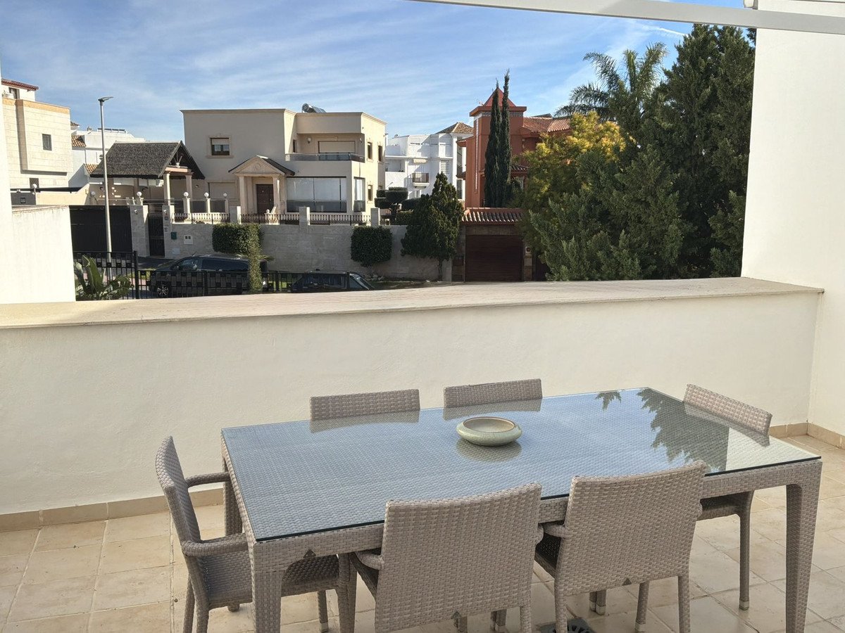 Terrace with dining set overlooking houses and trees under a bright blue sky.