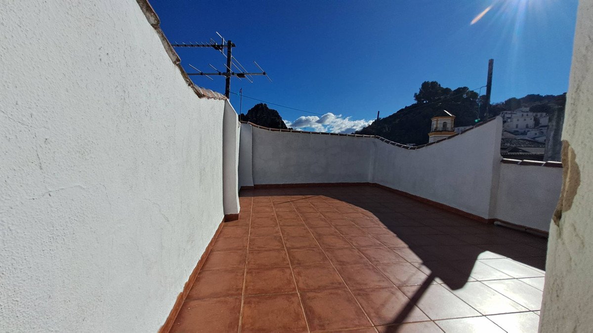 Tiled terrace with white walls overlooking a village nestled in green hills under a bright blue sky.