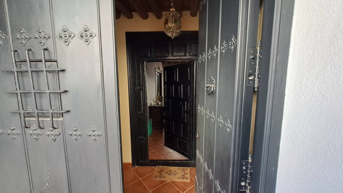 A dark metal entryway door opens to reveal a hallway with tiled floors and a decorative lantern hanging lantern.