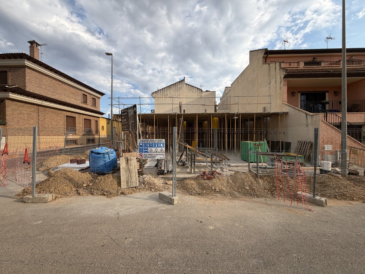 Exterior view of a property under construction, showing scaffolding, building materials, and surrounding houses.