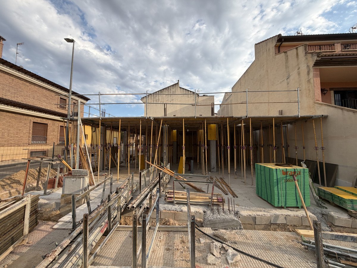 Construction site with scaffolding, wooden supports, and building materials under a cloudy sky.