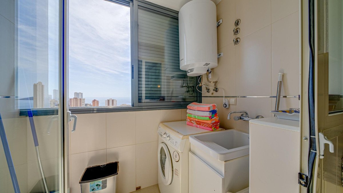 Bathroom with washing machine, sink, and city view through large window.
