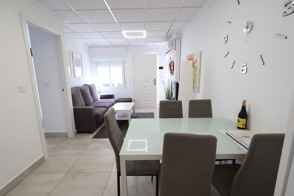 Modern living and dining area with sofa, coffee table, and dining set, featuring a large wall clock and bottle of wine.