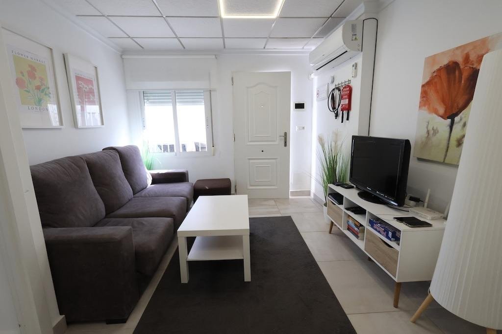 Cozy living room with a grey sofa, white coffee table, and TV entertainment center. Features floral art on the walls.