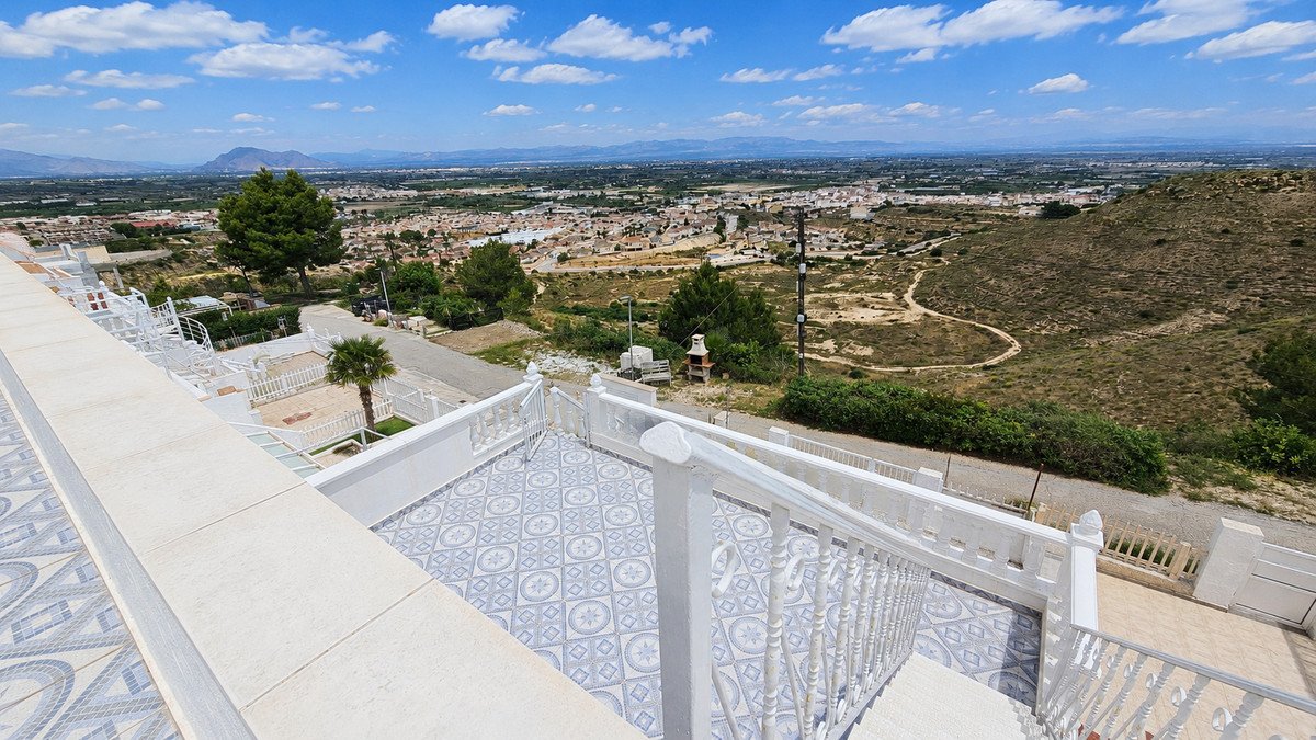 A white-railed terrace overlooks a town and valley under a blue sky with fluffy clouds. clouds.