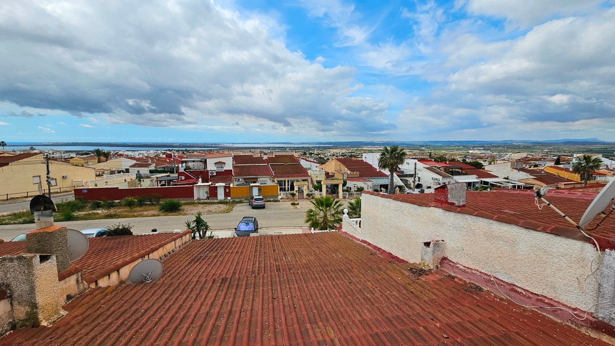 A panoramic view of a town with rooftops and a distant sea under a cloudy blue sky.