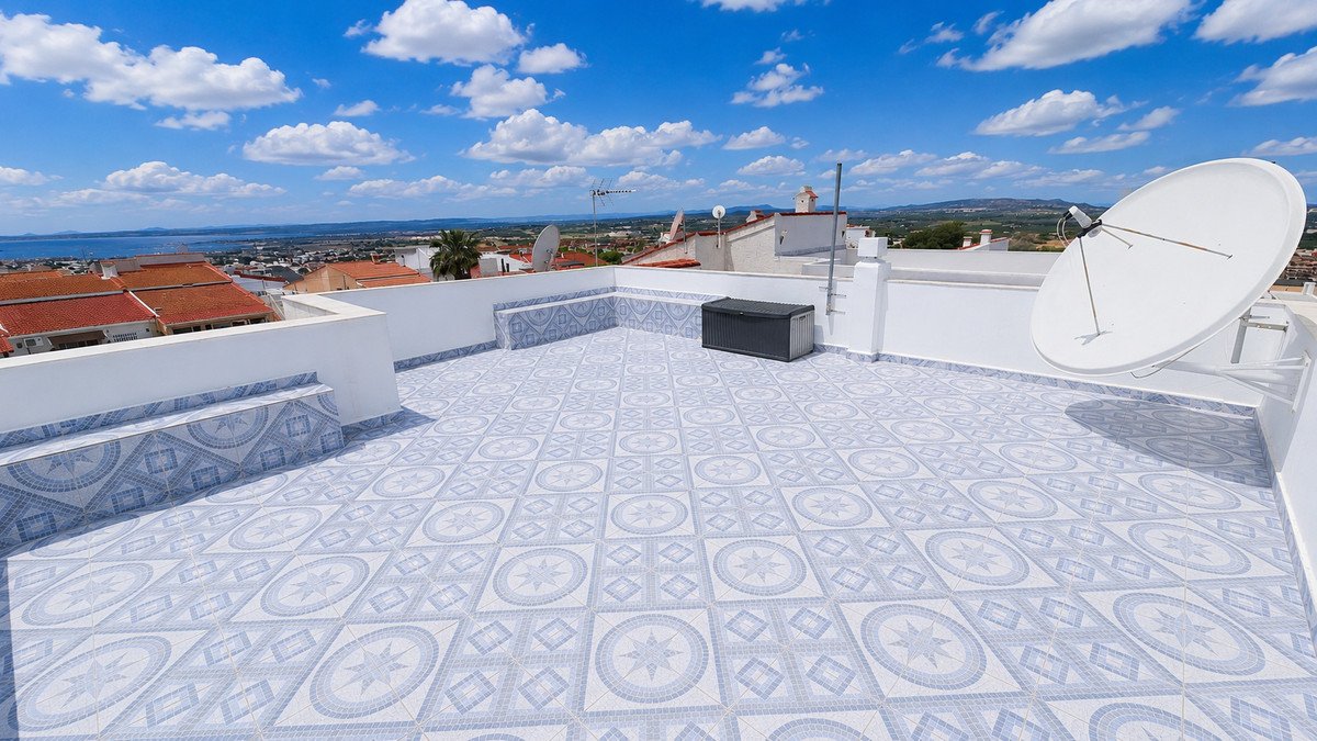 A spacious, tiled rooftop terrace with built-in seating, storage box, and satellite dish, offering panoramic views of the sea and town.