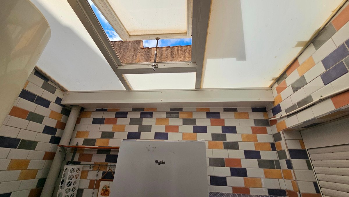 A covered terrace area with a skylight showing blue sky, colorful tiled walls, and a small refrigerator.