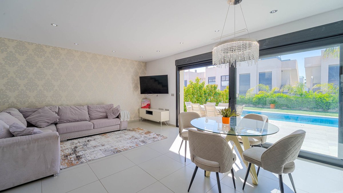 Modern living and dining area with a sectional sofa, TV, and a glass table, opening to a private pool and patio.